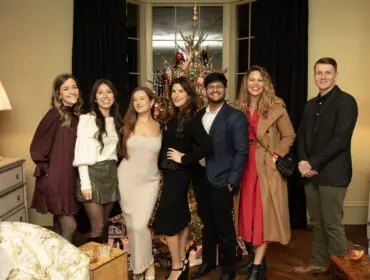 Seven people pose in front of a decorated Christmas tree.