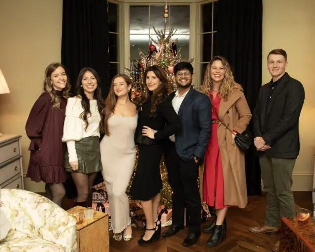 Seven people pose in front of a decorated Christmas tree.