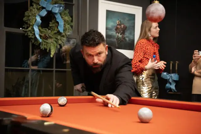 Man in black jacket playing pool with orange felt table.