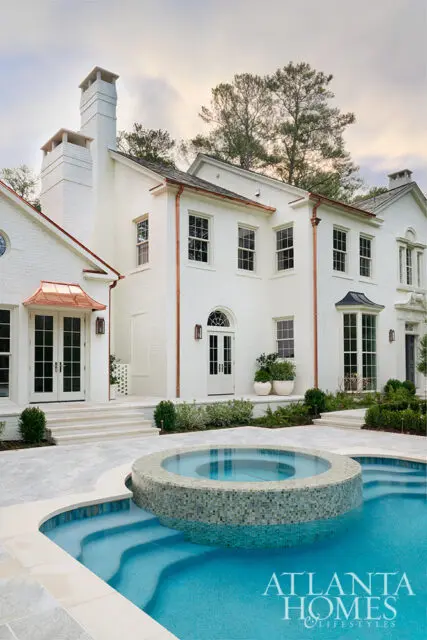 White brick house with copper gutters and a circular spa next to a swimming pool.