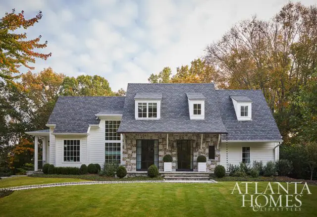 White house with stone accents, dormer windows, and manicured lawn. Atlanta Homes & Lifestyles logo