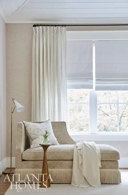 Chaise lounge with fringed base, patterned pillow, and gold side table.