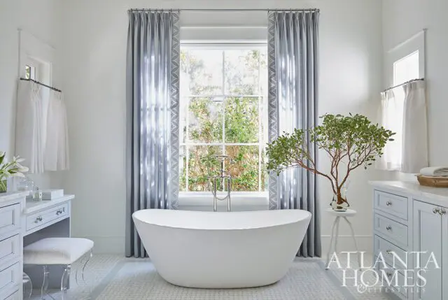 White freestanding bathtub with chrome faucet, flanked by gray cabinetry and a vanity.