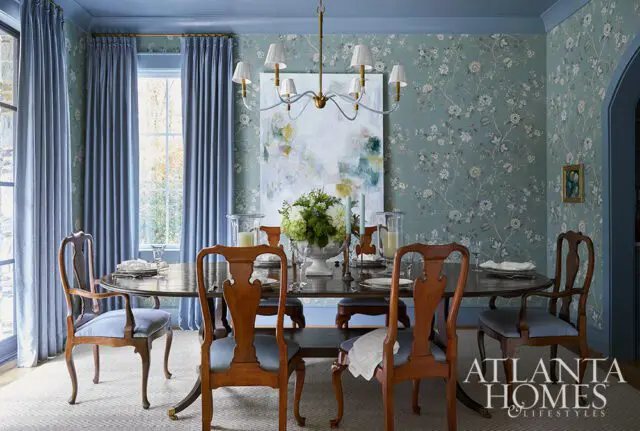 Dining room with floral wallpaper, blue curtains, and a table set for a meal.