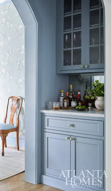 Blue bar cabinet with marble countertop, glass-front cabinets, and liquor bottles.