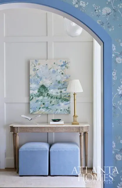 Entryway with paneled walls, marble console table, blue ottomans, and abstract art.