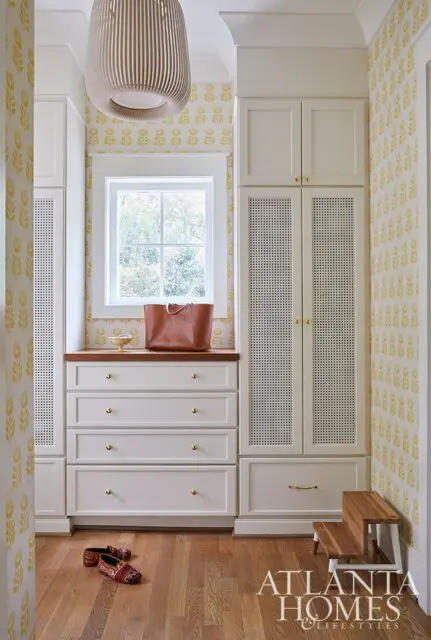 White built-in cabinets with cane detailing and yellow floral wallpaper.