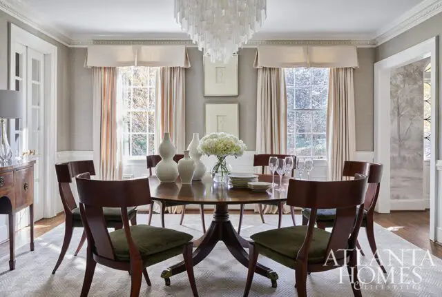 Dining room with round wood table, dark wood chairs with green seats, and large windows.