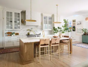 White kitchen with marble island, wood cabinetry, brass accents, and leather bar stools.