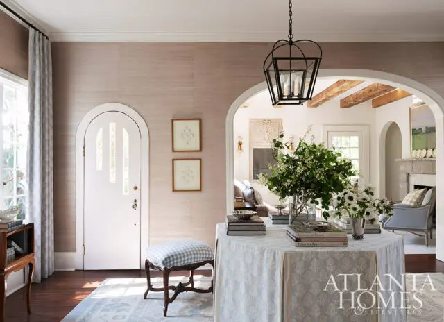 Entryway with grasscloth wallpaper, arched door, and table with floral arrangements.