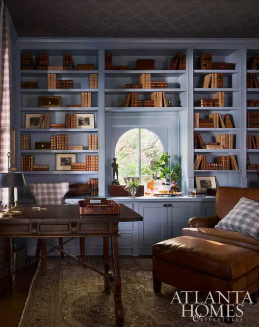 Blue built-in bookshelves filled with books, desk, leather armchair, and ottoman.