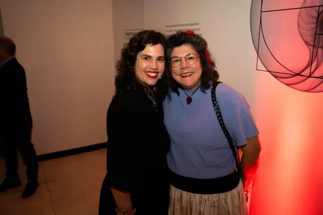 Two women smiling at the camera. The woman on the left wears a black top and the woman on the right