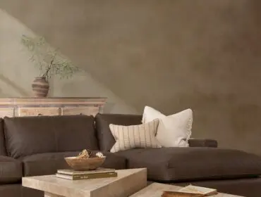 Brown leather sectional sofa with textured pillows and two stone coffee tables on a rug.