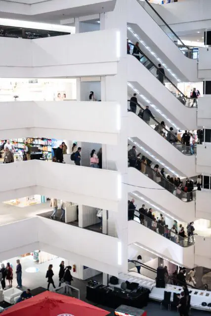 Multi-level interior with white architecture and escalators filled with shoppers.