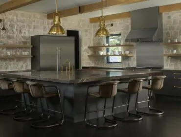 Kitchen with stone walls, dark cabinets, marble island, and brass pendant lights.
