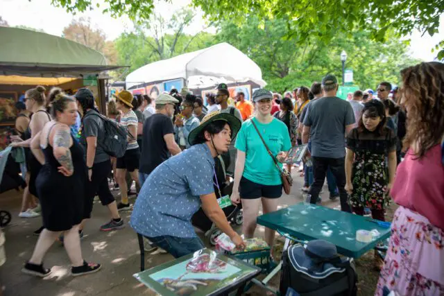 People at an outdoor art fair with tents and artwork visible.