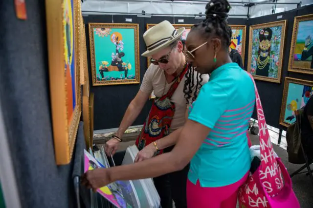 Two people examine artwork at an outdoor art fair.