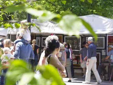People browsing art displayed under tents at an outdoor market.