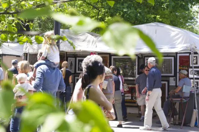 People browsing art displayed under tents at an outdoor market.