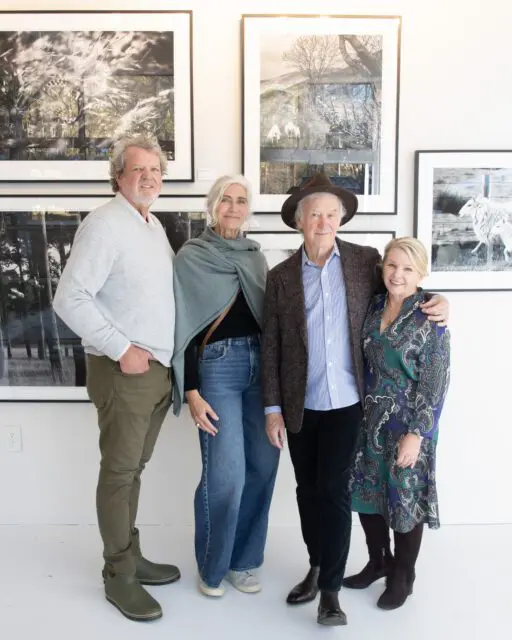 Four people standing in front of framed photographs on a white wall.