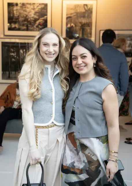 Two smiling women, one with blonde hair and a gray vest, the other with dark hair and a gray vest.