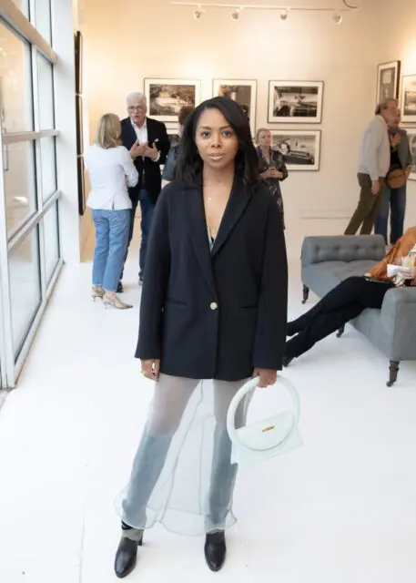 Woman in black blazer and sheer skirt holding a pale blue handbag.