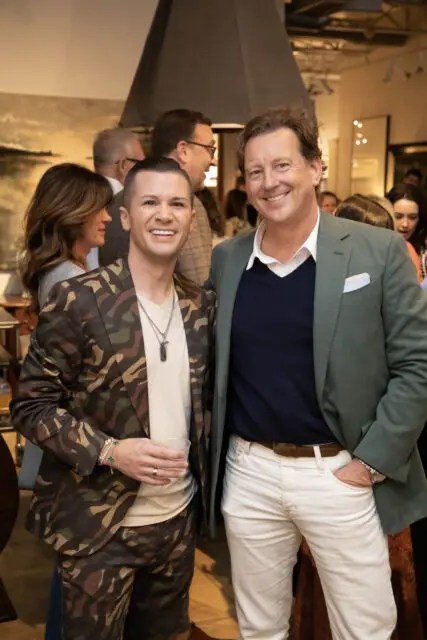 Two men smiling, one in a camouflage suit, the other in a green jacket and white pants.