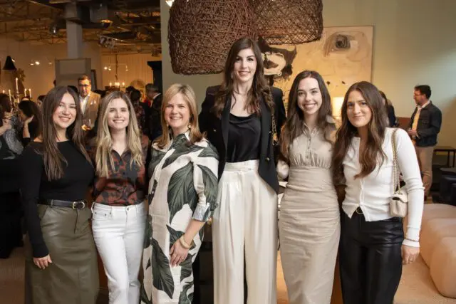 Six women posing indoors, with large woven light fixtures overhead.