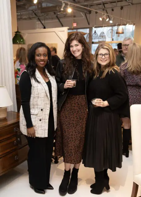 Three women posing indoors, one in a black and white tweed vest, one in a leopard print skirt, and