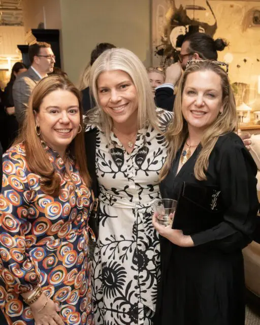 Three women smiling at the camera at an indoor event.