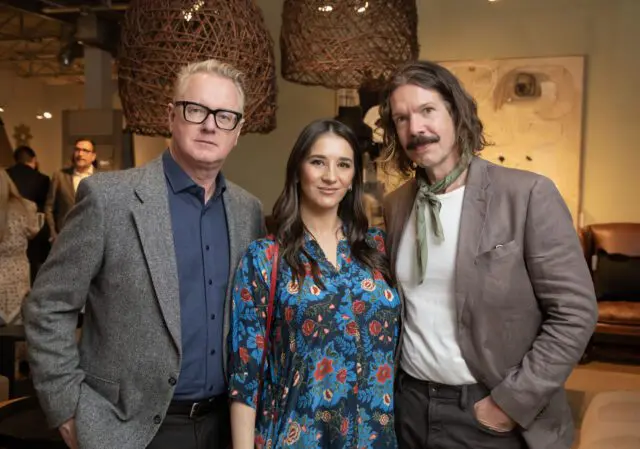Three people posing indoors with woven pendant lights overhead.
