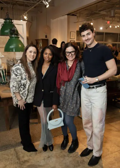 Four people posing indoors, two women and two men. The woman on the far left wears a black and