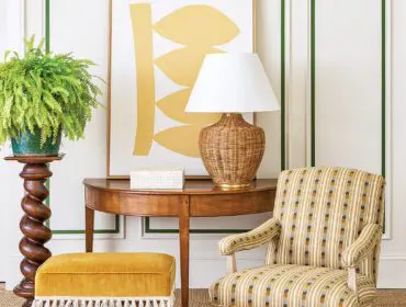 Armchair with striped upholstery, yellow ottoman with fringe, and wooden console table with lamp.