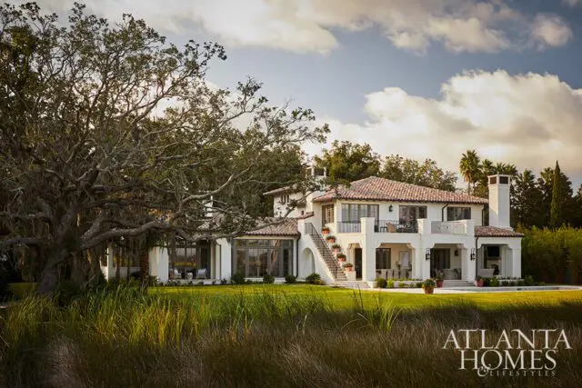 White Mediterranean-style house with red tile roof, balconies, and large oak tree