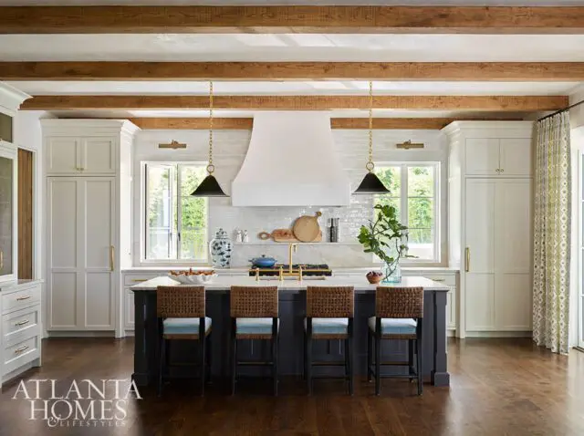 Kitchen with white cabinets, dark island, wood beams, and pendant lights.