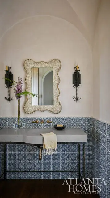 Powder room with concrete vanity, blue patterned tile, ornate mirror, and sconces