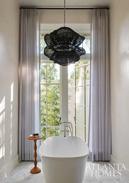 Freestanding bathtub with chrome fixtures under a black floral chandelier.