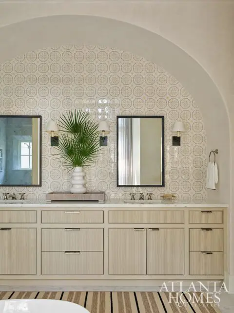 Bathroom with dual vanities, patterned tile backsplash, fluted cabinetry, and arched ceiling.
