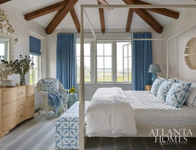 Bedroom with white four-poster bed, blue curtains, wicker chair, and coastal decor.