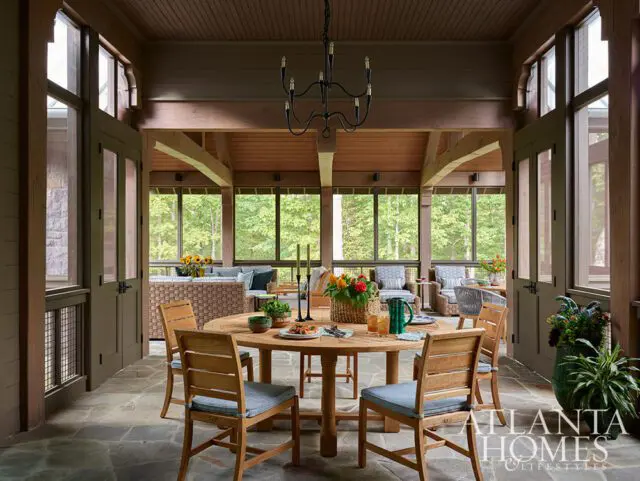 Screened porch with wood dining table, chairs, and wicker seating overlooking trees.