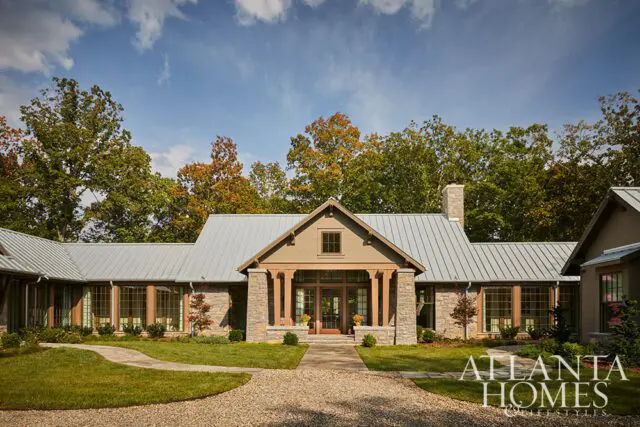 Stone and wood house with metal roof and large windows, surrounded by trees.
