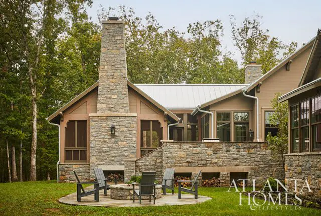 Stone house with large stone chimney, metal roof, and screened porch. Patio with fire pit and