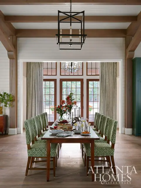 Dining room with wooden beams, green patterned chairs, and a table set for a meal.