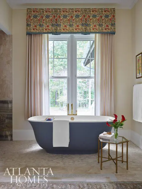 Dark blue bathtub with gold faucet, floral valance, and tiled floor.