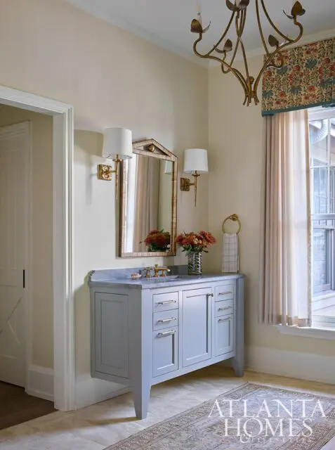 Powder room with light blue vanity, marble countertop, brass fixtures, and floral valance.