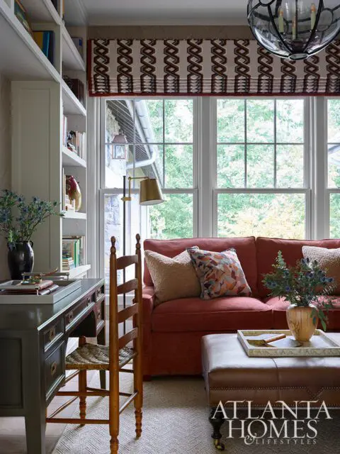 Red sofa with patterned pillows, leather ottoman, and desk with chair.