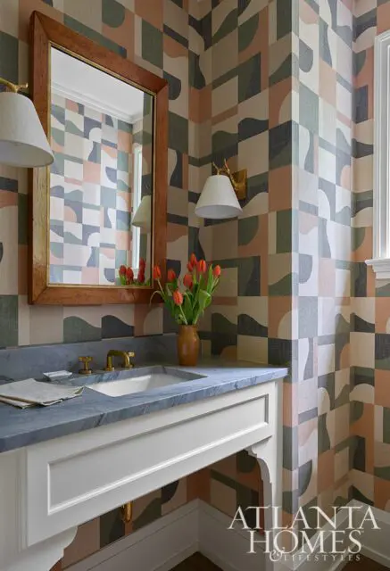 Powder room with geometric wallpaper, marble vanity, brass fixtures, and sconces.