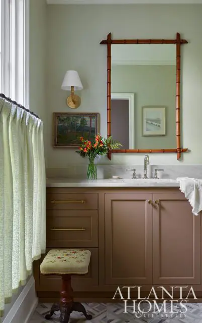 Powder room with taupe vanity, marble countertop, bamboo mirror, and floral stool.