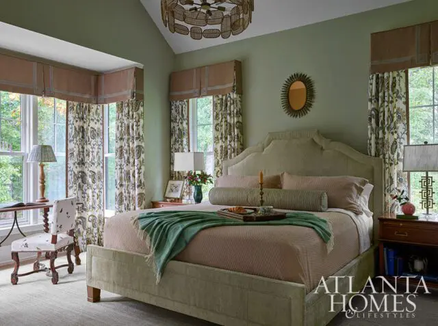Bedroom with green walls, upholstered headboard, patterned curtains, and a tray on the bed.