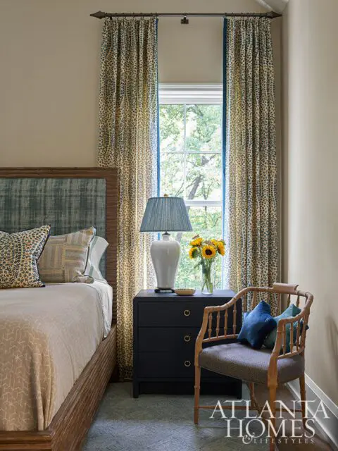 Bedroom with wood bed, patterned curtains, dark blue nightstand, and bamboo chair.